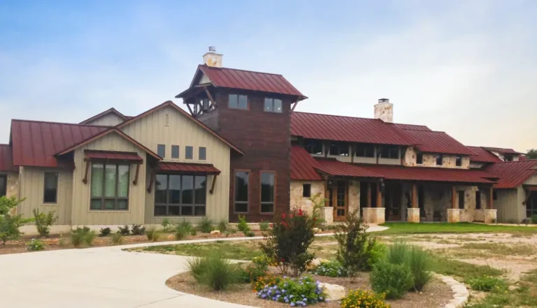 A large Hill Country style luxury home with a rust red metal roof, stone exterior, and native Texas landscaping