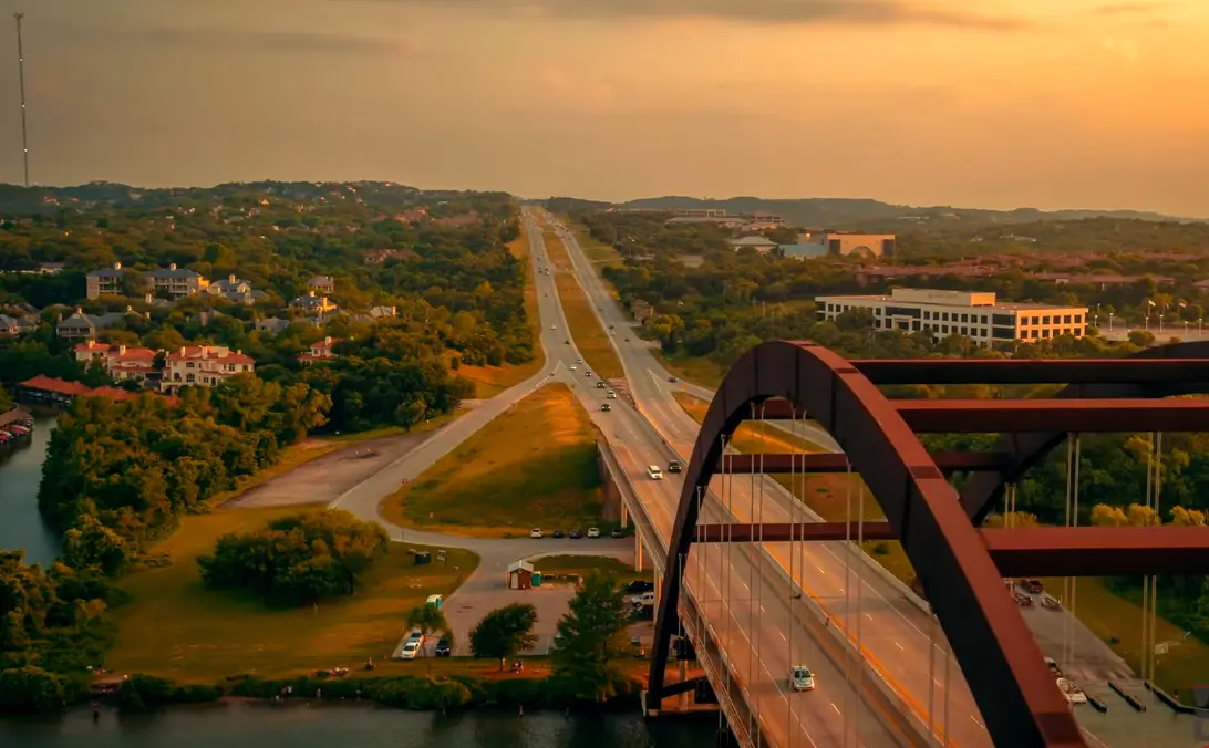 Aerial view of the 360 Pennybacker Bridge and Highway 360 in Austin, TX at sunset, with Lake Austin and Hill Country neighborhoods below