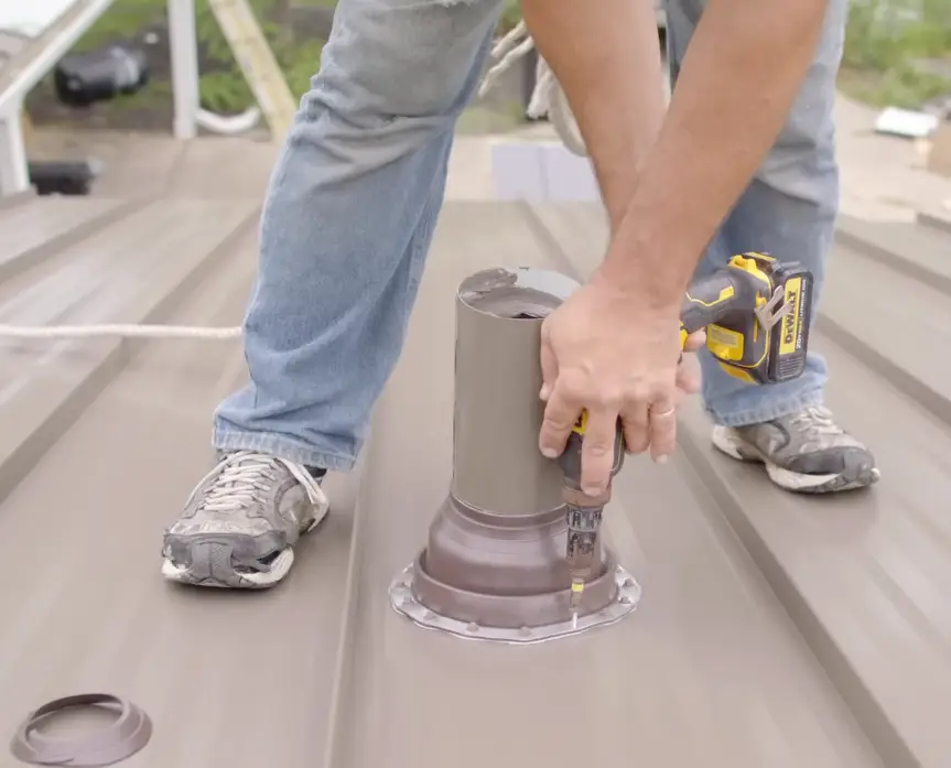 Roofer securing a pipe boot flashing on a standing seam metal roof with a drill