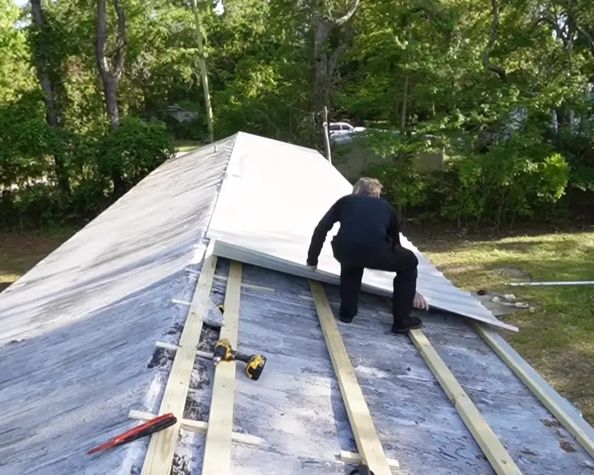 Roofer positioning a white metal panel over furring strips installed on an existing roof