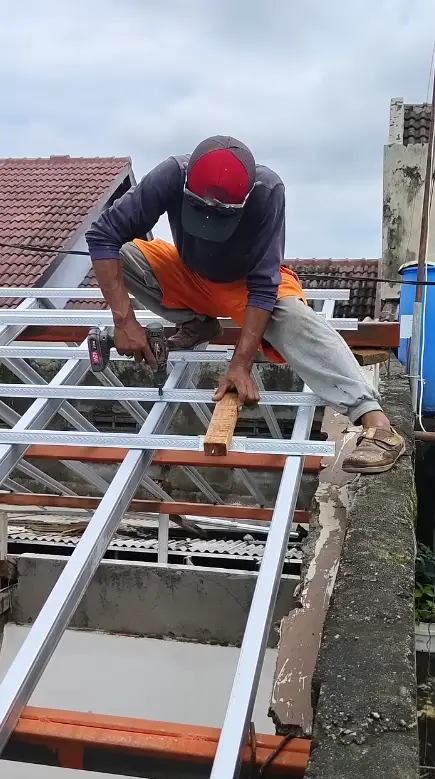 Roofing crew member drilling into a metal roof truss frame during installation on a rooftop
