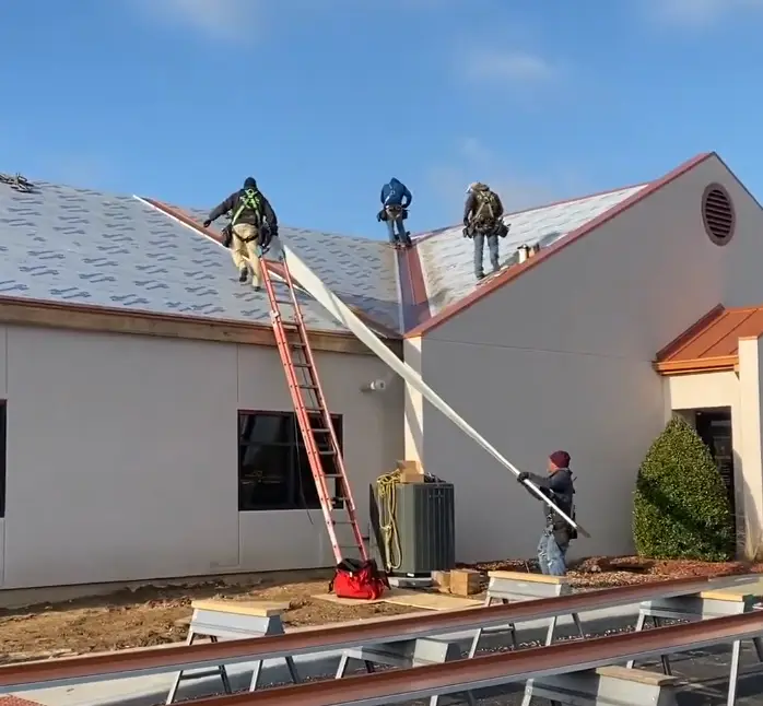 Roofing team of four installing metal panels on a building's peaked roof