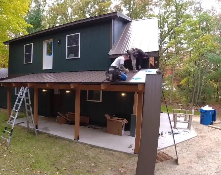 Roofing crew installing a brown standing seam metal roof over a covered porch during a home metal roof replacement