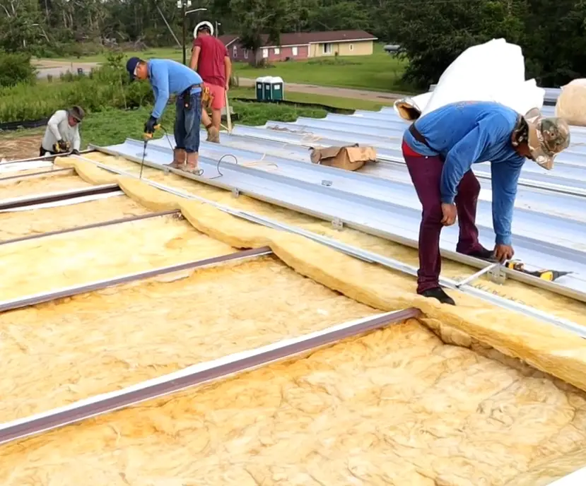 Roofing crew installing metal panels over insulation on a large commercial roof