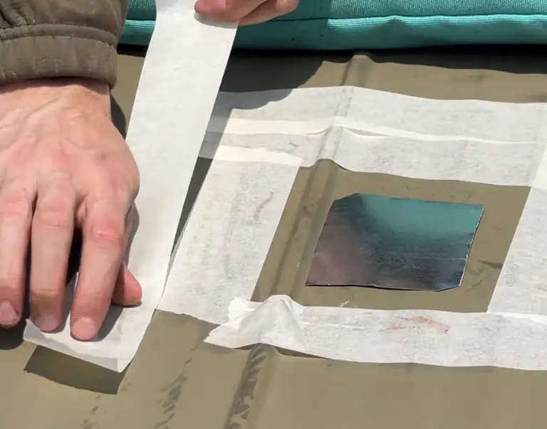 Roofer removing masking paper from a small metal patch applied to a roof panel