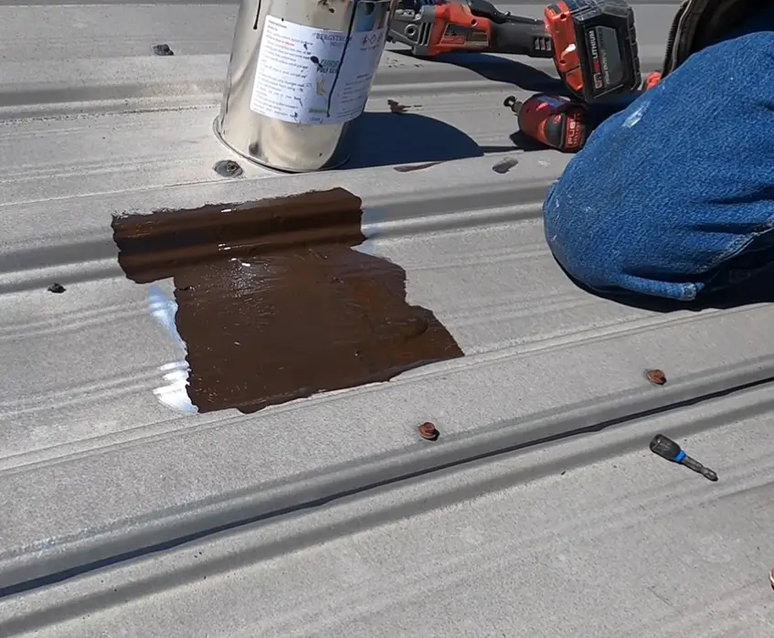 Roofer applying brown sealant coating to a section of a metal roof panel during maintenance