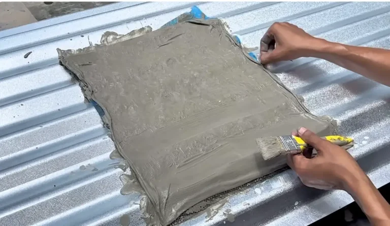 A large fiberglass mesh patch coated in gray sealant being applied to a corrugated metal roof panel