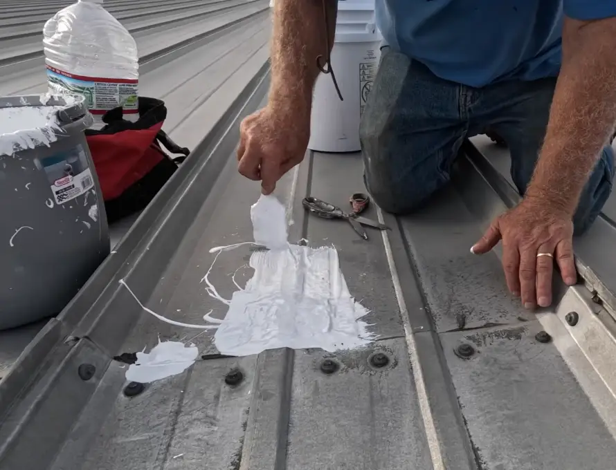 A roofer applies white sealant over a row of fasteners on a corrugated metal roof, addressing a visible warning sign before it leaks
