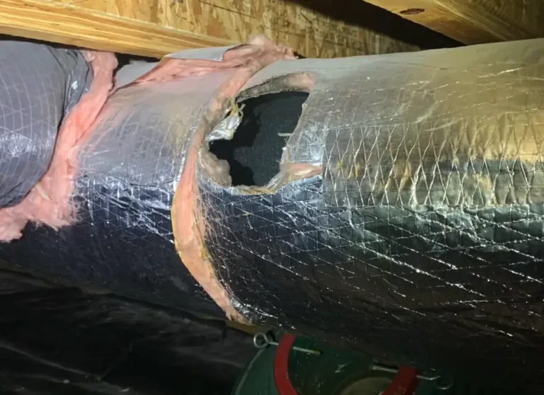 A damaged flexible HVAC duct with a torn opening exposing insulation inside an attic, the kind of issue a thorough attic check can catch