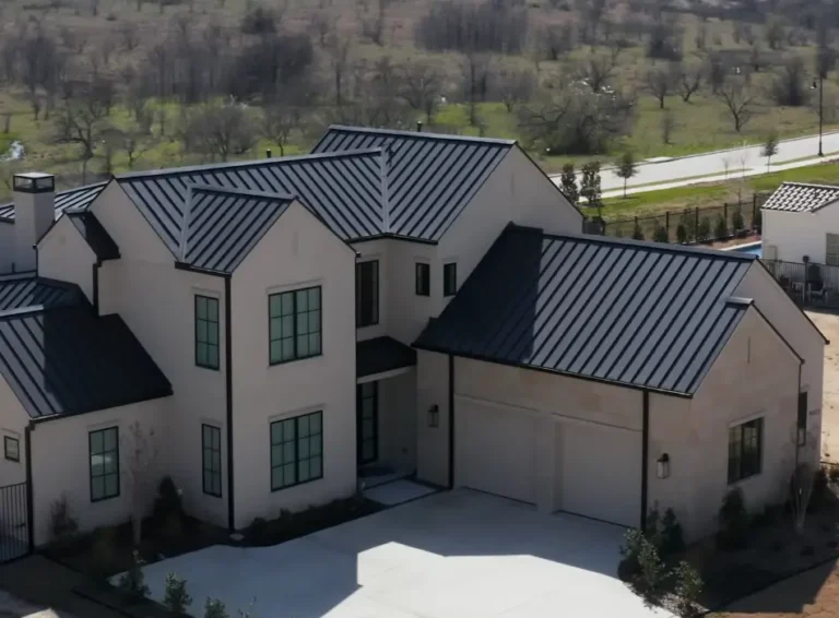 A large Hill Country style home with a dark standing seam metal roof and stone accents, seen from above with a neighboring pool visible