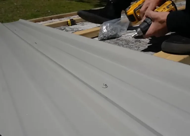 Close-up of a light gray metal roof panel being fastened with a drill, showing the exact fastener spacing that affects labor and materials cost