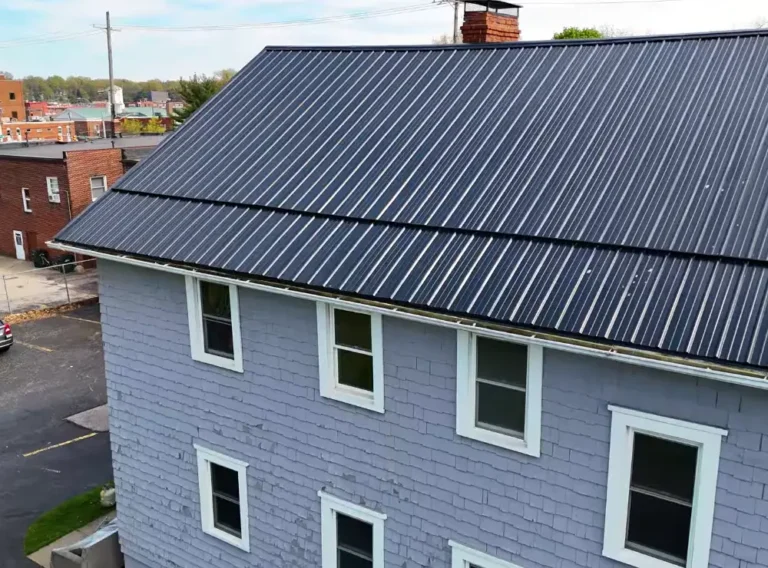 A large multi-story rental building with a dark standing seam metal roof and gray wood shingle siding, seen from above