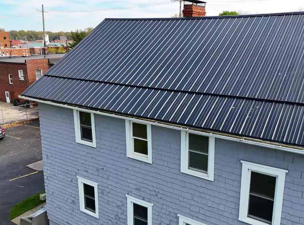 A large multi-story rental building with a dark standing seam metal roof and gray wood shingle siding, seen from above